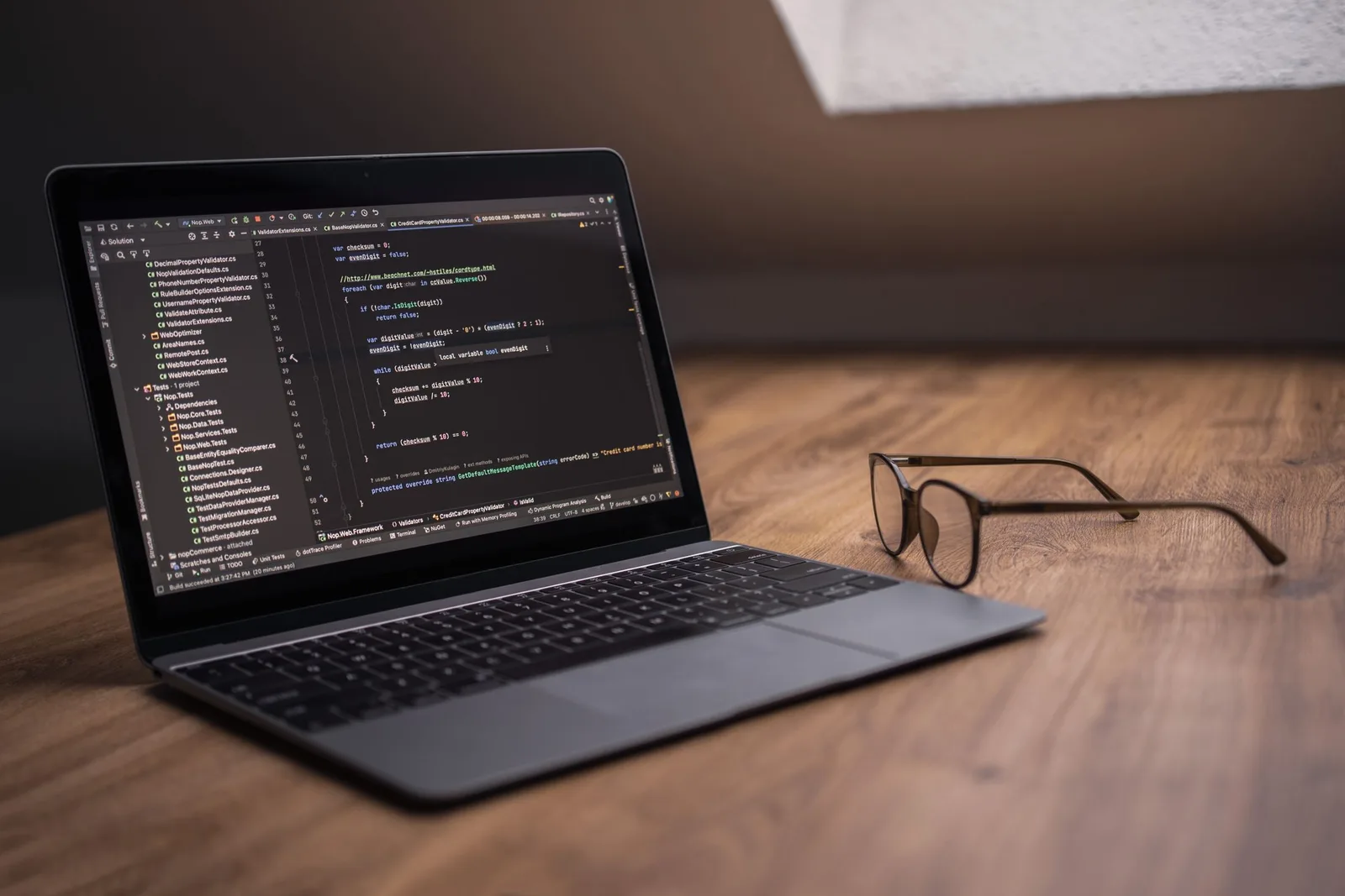 কাঠের desk-এ চশমার পাশে code editor খোলা laptop