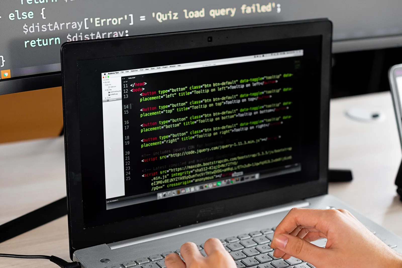 Laptop ও monitor-এ website code দেখে keyboard-এ কাজ করছেন একজন developer