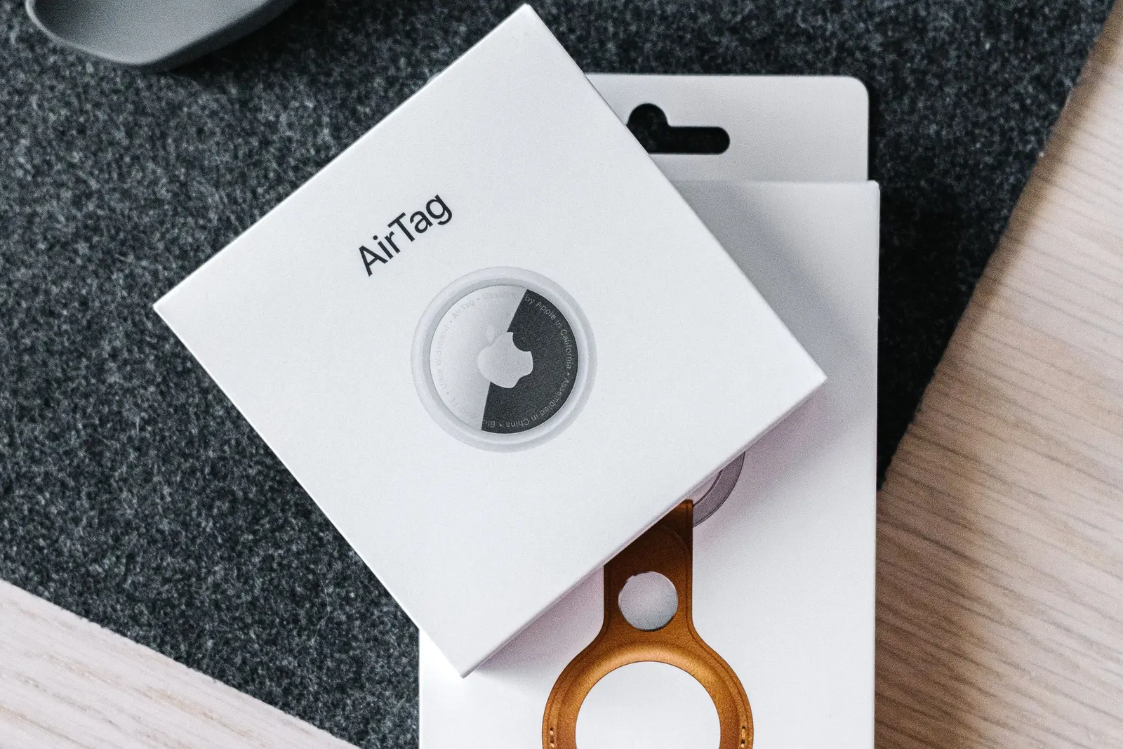 Wooden surface-এ AirTag tracking device ও leather key-ring-এর packaging