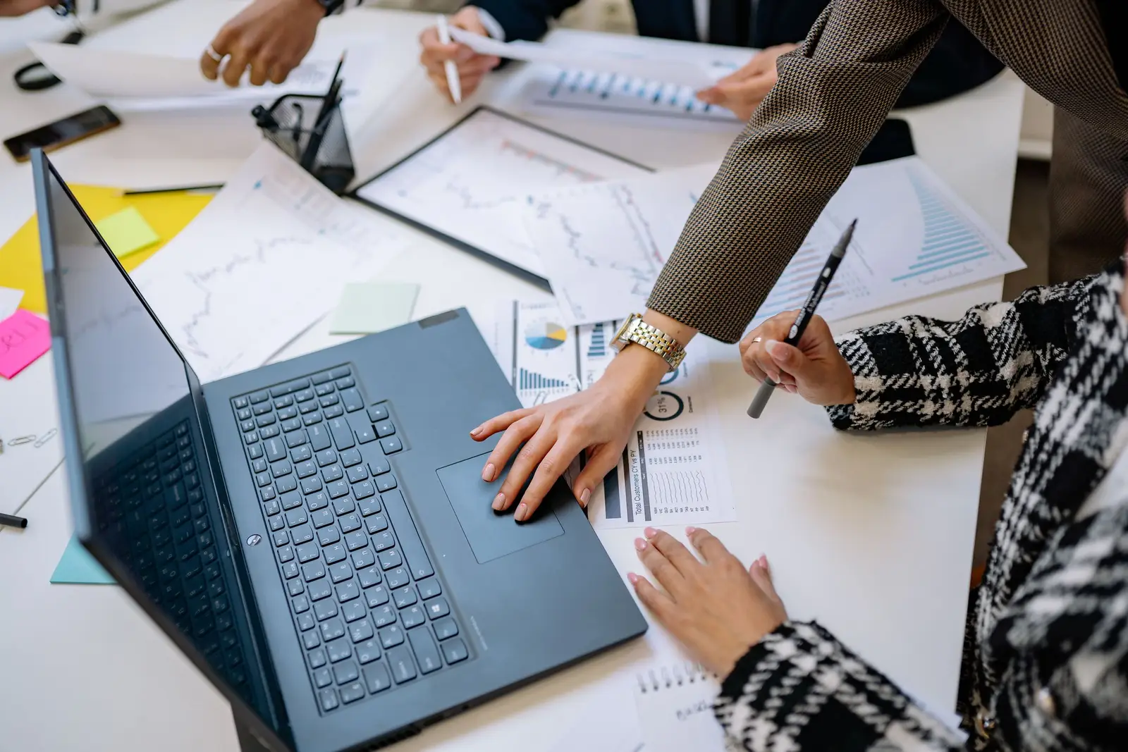 Meeting table-এ laptop ও chart দেখে AI output monitoring review করছেন একটি business team