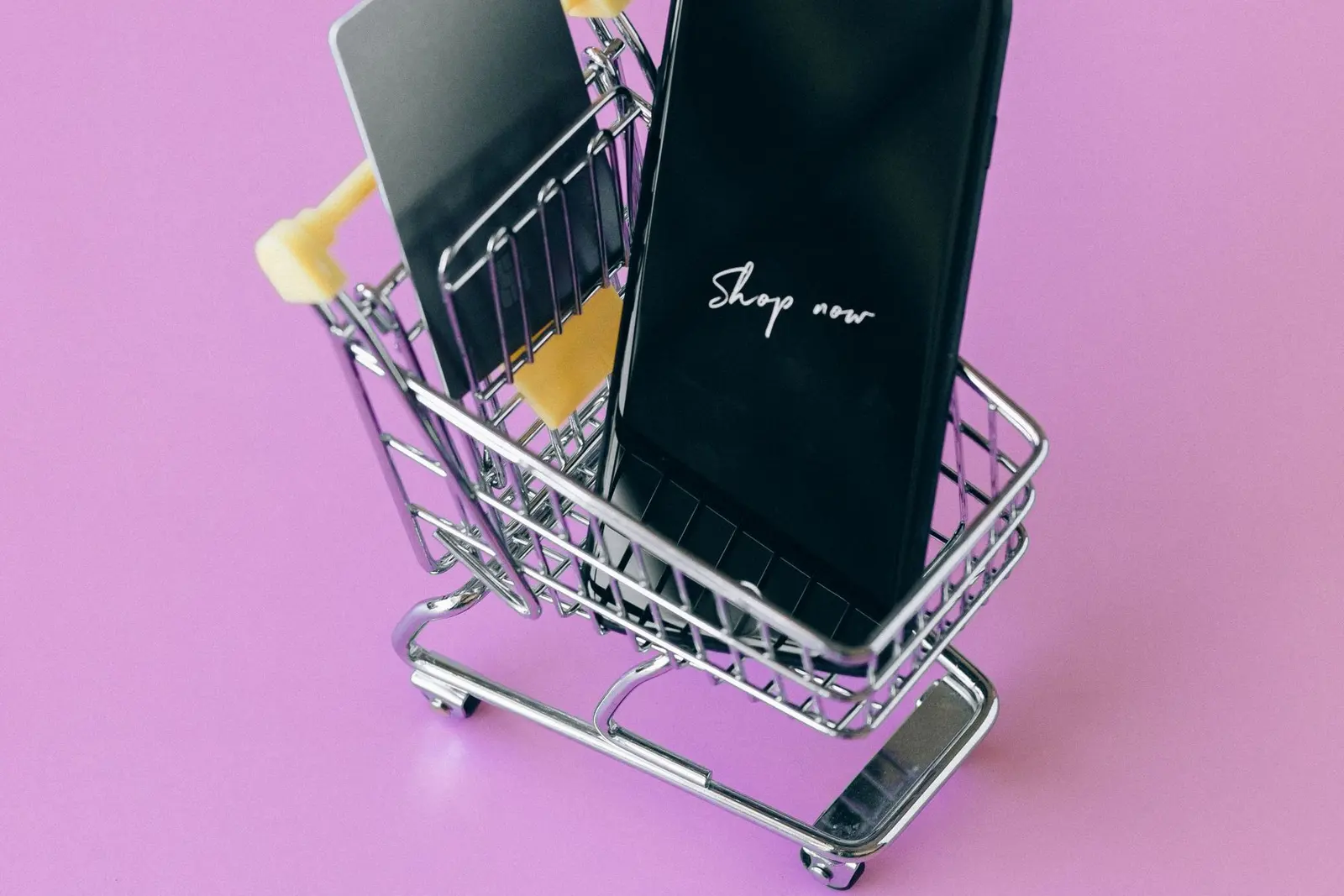 গোলাপি background-এ miniature shopping cart-এর মধ্যে smartphone ও payment card