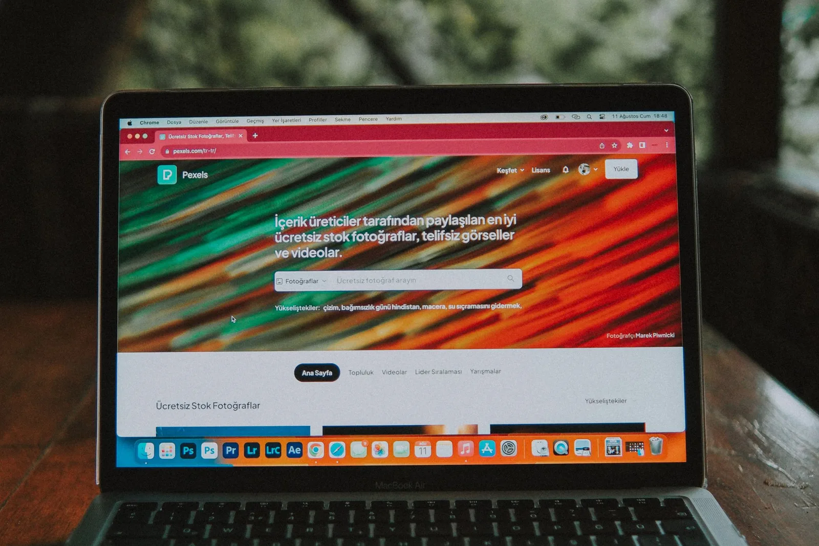 গাছপালার পাশে কাঠের table-এ browser খোলা laptop রাখা আছে