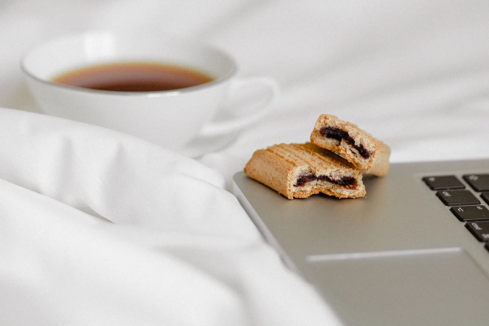 Laptop keyboard-এর পাশে biscuit ও tea রাখা একটি workspace