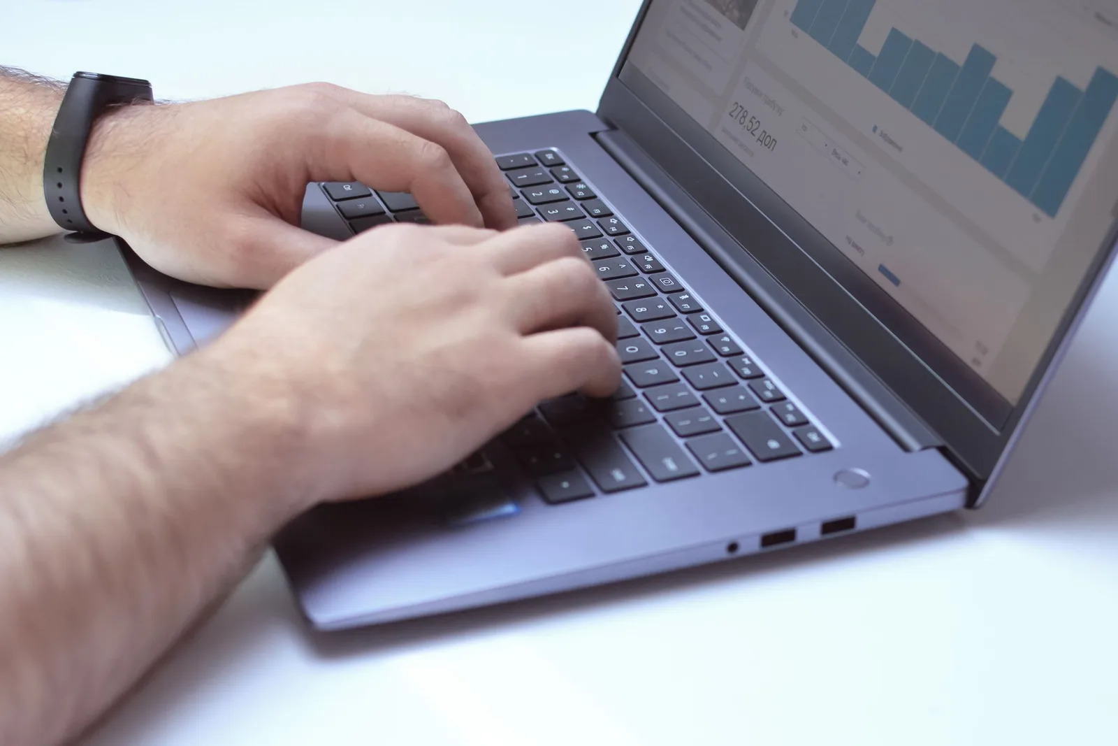 Laptop-এ data chart দেখে keyboard-এ কাজ করছেন একজন ব্যক্তি